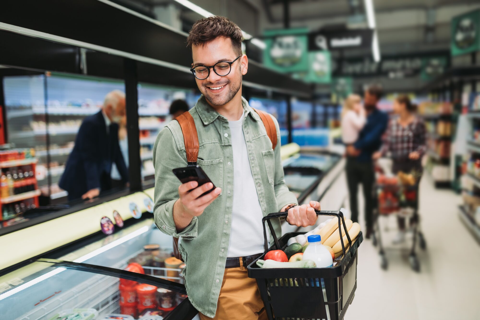 Man in a grocery store looking at his phone and smiling